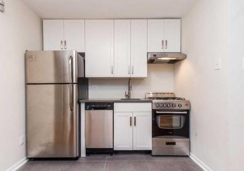 Updated kitchen with stainless steel appliances, grey tile flooring, and white shaker cabinetry.